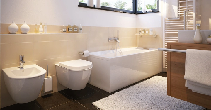 Ein weißes Badezimmer zeigt ein Bidet und eine Toilette, mit einer Badewanne daneben. Regal mit Flaschen im Hintergrund helle Wände und eine Fensteransicht. Teppich auf dem Boden.