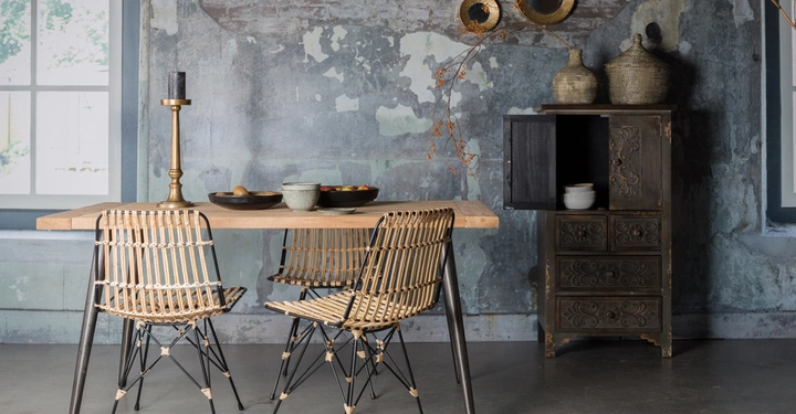 Galerie-Bild 3: Zwei Rattanstühle und ein Holztisch mit Schalen darauf stehen vor einer verwitterten Wand zwei runde Wandspiegel hängen oben rechts Ein hölzerner Schrank mit Vasen steht daneben Fenster im Hintergrund.