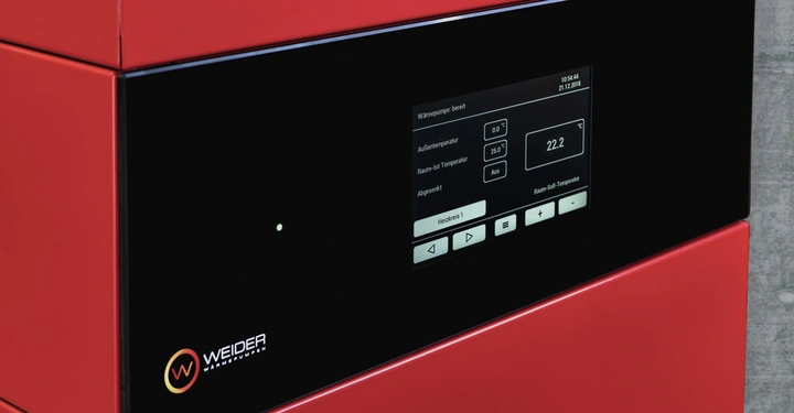 Digitaler Bildschirm zeigt Heizungssteuerung in moderner roter Wärmepumpe im Innenbereich. Text: Wärmepumpe bereit, Außentemperatur, 0.0°, Raum-Ist Temperatur, 25.0°, Raum-Soll-Temperatur, 22.2°C. Zeit 10:56:44, Datum 21.12.2018, WEIDER WÄRMEPUMPEN.