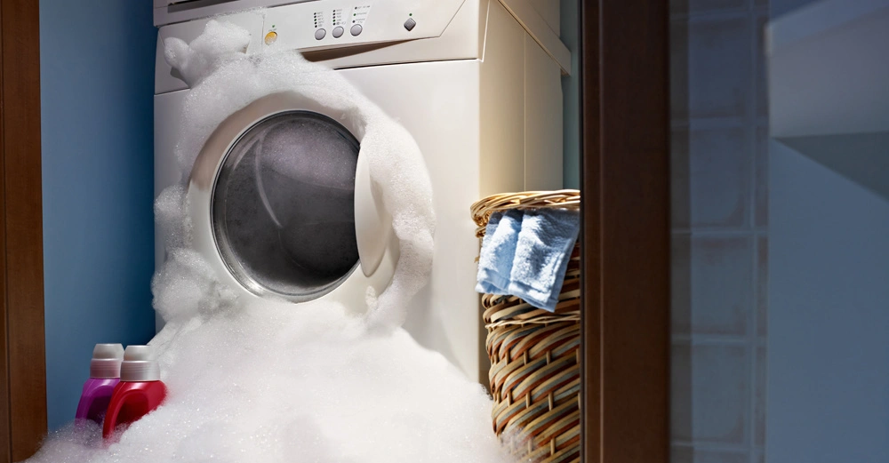 Wasserschaden! Waschmaschine in Waschküche, aus der dicke Schichten Schaum und Wasser quellen