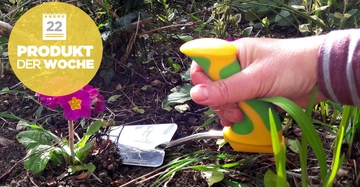 Hand hält Gartengerät, gräbt Erde neben lila Blume, umgeben von Grünpflanzen Text auf gelbem Kreis 22 PRODUKT DER WOCHE