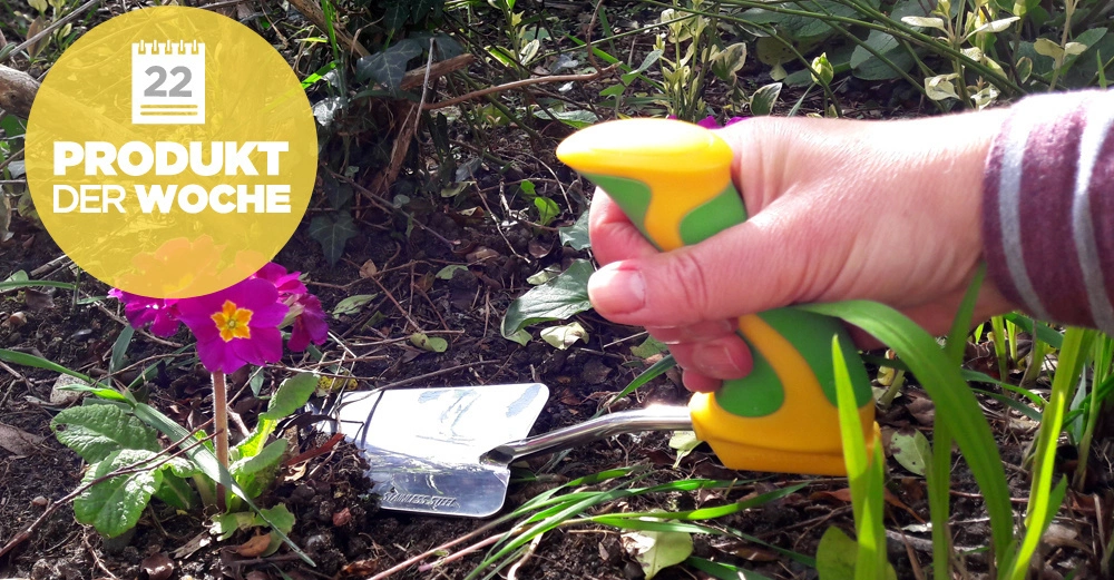 Hand hält Gartengerät, gräbt Erde neben lila Blume, umgeben von Grünpflanzen Text auf gelbem Kreis 22 PRODUKT DER WOCHE