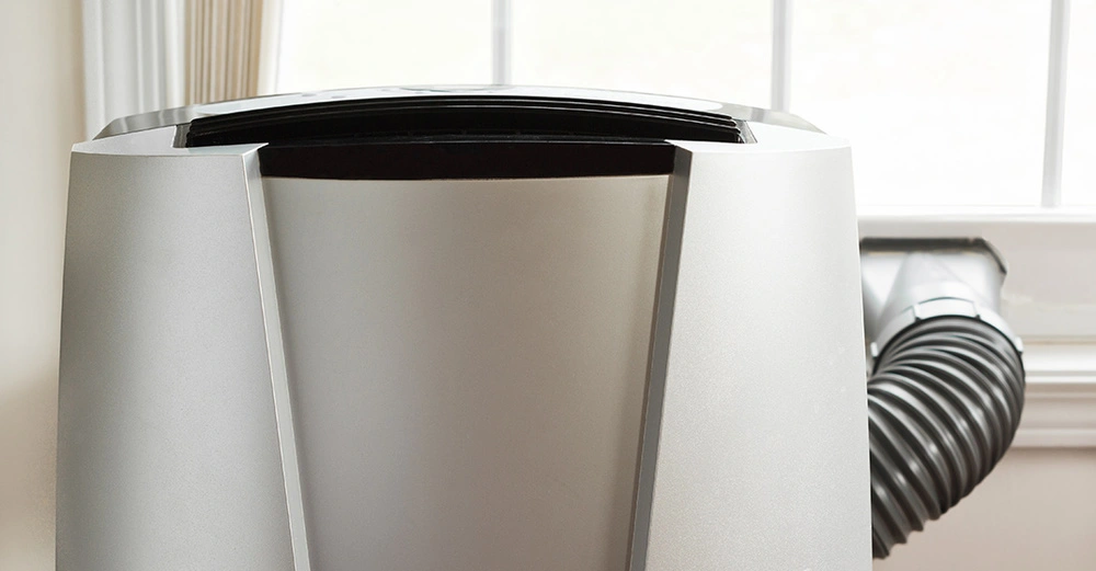 Mobiles Klimagerät vor hell erleuchtetem Fenster zur flexiblen Raumkühlung im Sommer.