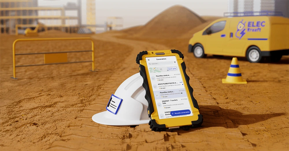 Symbolbild: Handy in schwarz-gelber Schutzhülle mit der Baustellenmanagement-App von Kraaft liegt auf dem sandigen Boden einer Baustelle. Im Hintergrund ist ein gelber Wagen zu sehen.