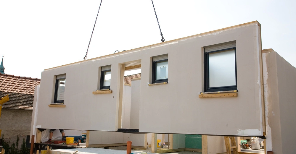 Hauswand wird mit Kran in Position gehoben Baustellenumgebung mit unfertigen Strukturen und Arbeiter im Hintergrund