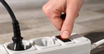 Hand drückt Schalter auf weißer Steckdosenleiste Kontext unscharfer Hintergrund in Innenraumumgebung.