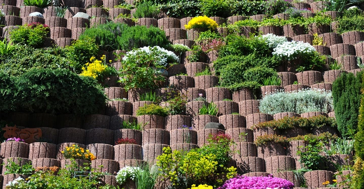 Blühende Pflanzen wachsen in mehreren Ebenen von Terrakotta-Blöcken in einem vertikalen Garten. Die Blöcke sind symmetrisch angeordnet und bilden eine üppige und farbenfrohe Wandstruktur.