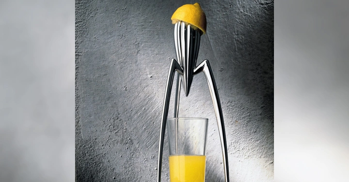 Galerie-Bild 8: Zitronenpresse aus Metall klemmt eine halbe Zitrone und presst Saft in ein Glas vor grauer Wand in Küchenumgebung