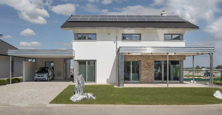 Ein modernes zweistöckiges Haus mit Solarpanelen auf dem Dach steht in einer Vorstadtumgebung Ein Auto parkt in einem Carport auf der linken Seite vor dem Haus Der Himmel ist wolkig