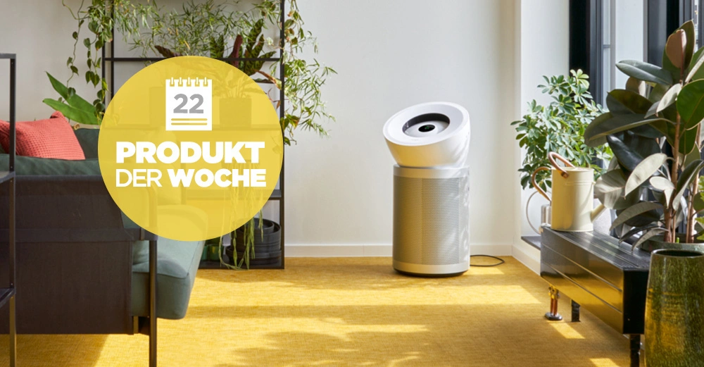 Luftreiniger steh auf einem gelben Teppich in einem hellen Wohnzimmer mit Pflanzen und Möbeln. Text im Bild: 22 PRODUKT DER WOCHE.