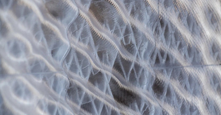 Durchsichtige, gekräuselte Plastikfolie mit diagonalen, wellenartigen Mustern. Unter starkem Licht erzeugt die Struktur eine Vielzahl von Licht- und Schatteneffekten, die an ein kompliziertes Netzwerk erinnern.