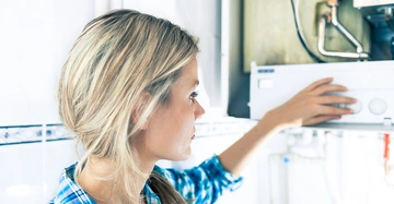 Eine Frau dreht an einem Heizungsregler in einem hellen Raum mit weißen Wänden und Fliesen im Hintergrund.