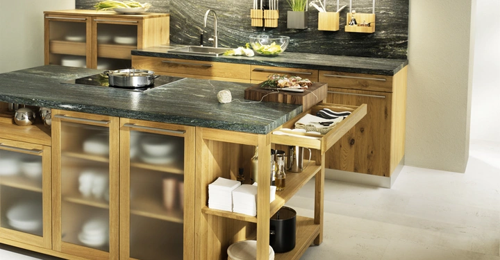 Galerie-Bild 9: Eine moderne Küche mit Holzmöbeln Arbeitsplatten aus dunklem Stein und vielen Regalen Küchenutensilien und Zutaten sind um die Spüle und das Kochfeld angeordnet.