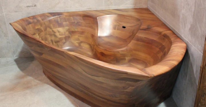 Galerie-Bild 4: Eine Holzbadewanne steht in einer Ecke eines Badezimmers aus beigen Fliesen. Text auf der linken Fliese lautet vavv.at.