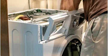 Mann hat Waschmaschine zerlegt und arbeitet an der entfernten Front mit Schraubenzieher.