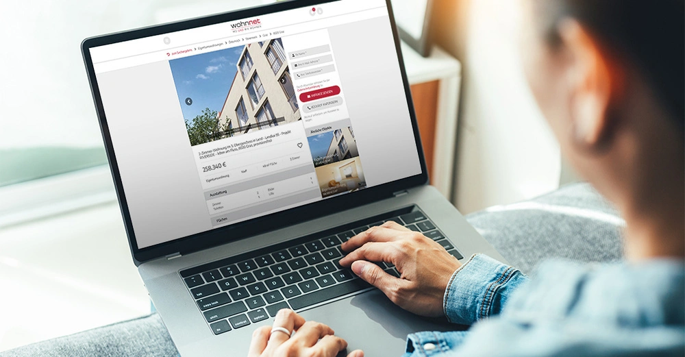 Person tippt auf Laptop und schaut sich Immobilienangebot auf wohnnet.at an mit Preisangabe von 258,34 Euro pro Monat und Details zur Wohnung in einem hellen Raum bei Tageslicht