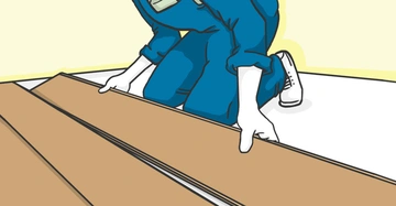 Eine Person in blauer Kleidung kniet und legt Holzbretter auf einen weißen Boden in einem Raum mit hellgelben Wänden.