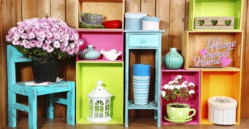 Blumen und Dekorationen platziert auf bunten Regalen und einem türkisfarbenen Stuhl vor einer Holzwand Die Regale enthalten Vasen Tassen Körbe und einen Schriftzug Home Sweet Home