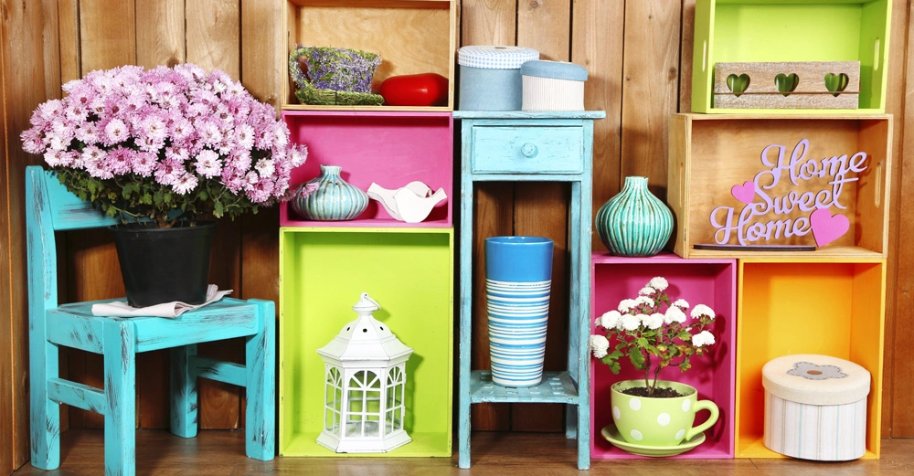 Blumen und Dekorationen platziert auf bunten Regalen und einem türkisfarbenen Stuhl vor einer Holzwand Die Regale enthalten Vasen Tassen Körbe und einen Schriftzug Home Sweet Home