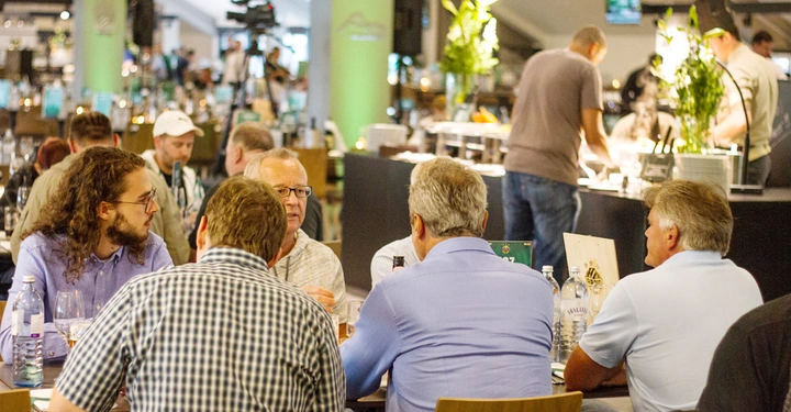 Galerie-Bild 4: Personen unterhalten sich am Tisch in lebhaftem Restaurantumfeld mit Bedienung im Hintergrund.