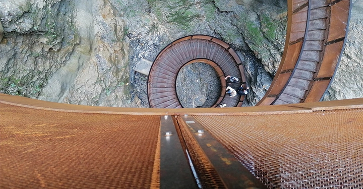 Galerie-Bild 9: Spiralförmige Treppe wird von Menschen hinuntergegangen felsige Umgebung mit grünen Flechten und Gestein