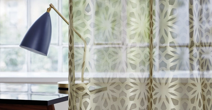 Galerie-Bild 14: Lampe steht auf einem Tisch leuchtet durch ein durchsichtiges Vorhangmuster und befindet sich vor einem großen Fenster mit geometrischer Struktur.