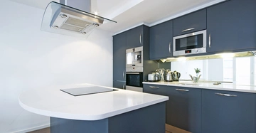 Eine moderne Küche mit dunkelgrauen Schränken Küche verfügt über einen Herd auf einer weißen Insel-Arbeitsplatte und eine eingebaute Mikrowelle und Kaffeemaschine Edelstahlkanne im Hintergrund heller Raum.