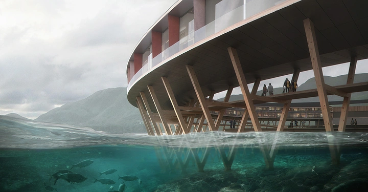 Galerie-Bild 1: Halbrundes Gebäude erhebt sich auf Stelzen über dem klaren Wasser Ein paar Leute stehen auf einer Terrasse Berge liegen im Hintergrund Fische schwimmen unter Wasser