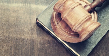 Ein Holzrichterhammer liegt auf einem schwarzen Buch auf einem Holztisch