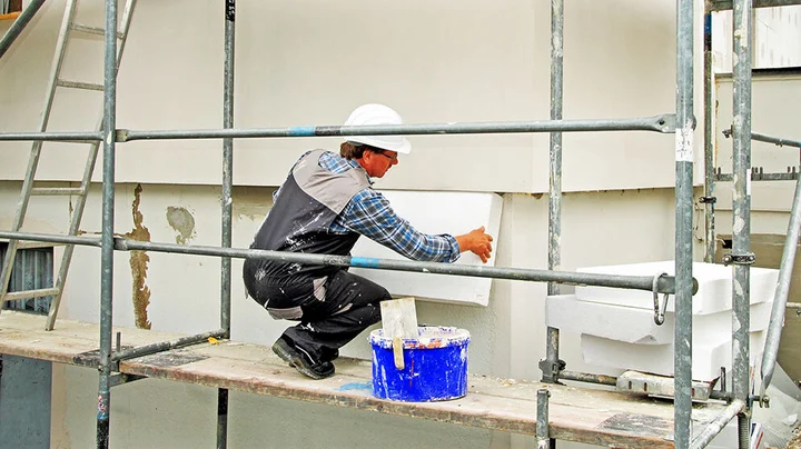 Ein Handwerker auf einem Fassadengerüst installiert einen Vollwärmeschutz aus Styroporplatten an der Hausfassade