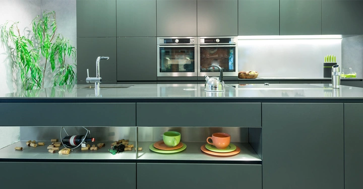 Küche im Industrial Style mit dunkelgrün-grauen Fronten. Im Vordergrund ein Regal mit hellgrünen und orangen Teetassen, die das Bild optisch aufpeppen.