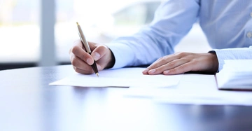 Mann in weißem Hemd unterzeichnet einen Bescheid an seinem eleganten Schreibtisch mit hochwertigem Kugelschreiber