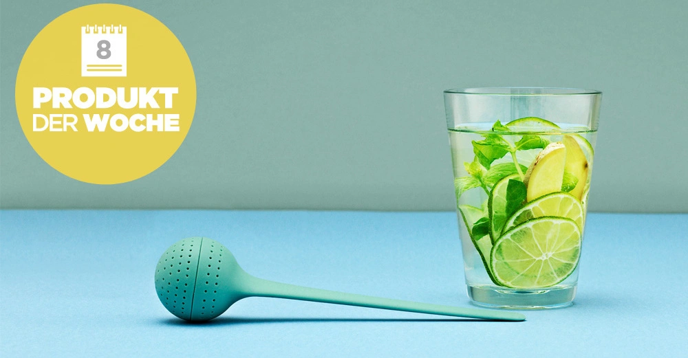 Grünes Teesieb liegt auf blauem Untergrund neben einem Wasserglas mit Zitronenscheiben und Minzblättern in minimalistischer Umgebung. Gelber Kreis mit Text PRODUKT DER WOCHE und Kalenderzahl 8.