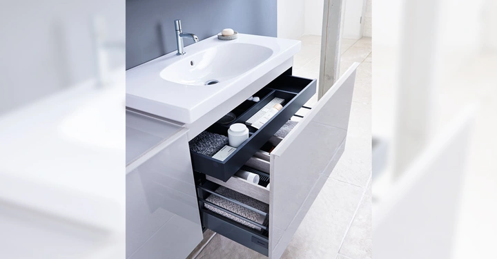 Galerie-Bild 5: Ein modernes Waschbecken mit Wasserhahn öffnet eine Schublade mit Handtüchern und Pflegeprodukten im Badezimmer mit hellen Fliesen und einem großen Spiegel.