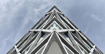 Gebäudeecke ragt geometrisch in den Himmel moderne Architektur beton graue und gläserne Strukturen diagonale Verstrebungen umgeben von blauem Himmel und dünnen Wolken