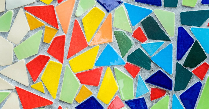 Bunte Dreiecksmosaikfliesen liegen zufällig auf einer grauen Unterlage. Die Dreiecke sind in verschiedenen Farben wie Rot, Blau, Gelb, Grün und Orange zu sehen.