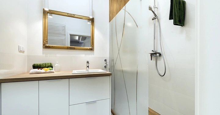 Waschbecken mit gold-gerahmtem Spiegel in modernem Badezimmer und einer Dusche mit Glaswand rechts daneben Handtücher auf der Arbeitsfläche