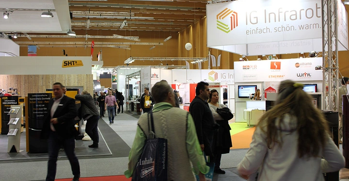 Galerie-Bild 6: Mehrere Menschen gehen durch eine Messehalle mit verschiedenen Ständen im Hintergrund. Ein markanter Stand mit dem Logo IG Infrarot und dem Text einfach. schön. warm. ist sichtbar.