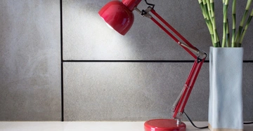 Rote Schreibtischlampe beleuchtet Tischoberfläche neben hoher Vase mit Bambus im modernen grauen Raum.