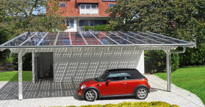 Rotes Auto parkt unter Carport mit transparentem Dach mit Sonnenkollektoren Fahrräder in Carport Gras Bäume und Haus mit rotem Dach im Hintergrund