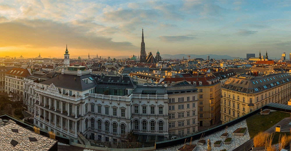 Gebäude stehen ruhig umgeben von weiteren Stadtstrukturen und Kirchtürmen im Hintergrund bei Sonnenuntergang während die sanfte Abendsonne den Himmel in warmen Orange und Blau taucht