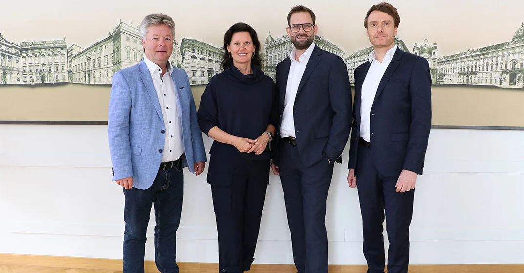 Drei Männer und eine Frau stehen vor einer großen Wand mit Gebäuden auf großer Leinwand.