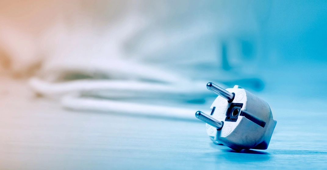 Weißer Stromstecker mit Kabel liegt auf einem Tisch, Nahaufnahme mit unscharfem Hintergrund, Symbol für Strom, Energie und Haushaltsgeräte.