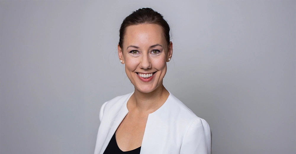 Dorner, Mitte 40, steht vor grauem Hintergrund und lächelt in weißem Businesssakko in die Kamera. 