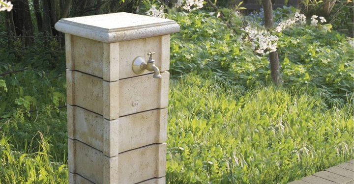 Galerie-Bild 5: Steinsäule mit Wasserhahn in einem grünen Garten mit Bäumen und blühenden Sträuchern im Hintergrund.