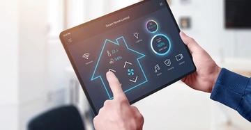 Großaufnahme eines Tabletts mit Smart Home Menü, Mann tippt auf eine Funktipon, im Hintergrund Wohnzimmer in hellen Farben