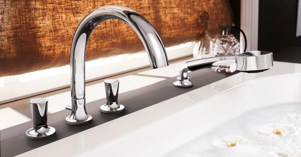 Ein verchromter Wasserhahn füllt eine Badewanne, die von schwimmenden weißen Blüten und Schaum umgeben ist; dahinter ist ein brauner Vorhang.