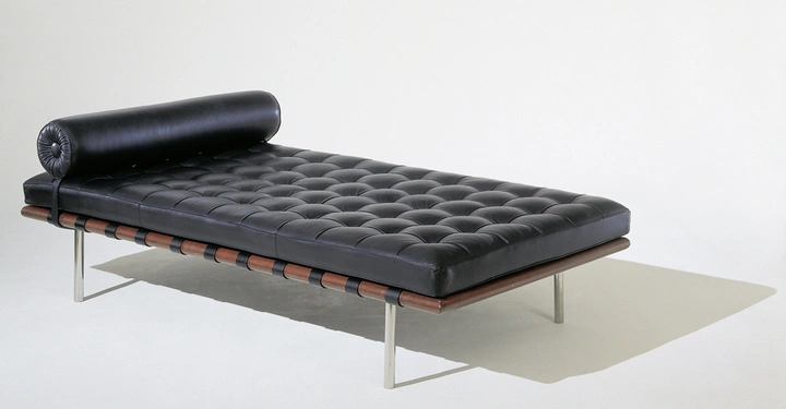 Galerie-Bild 3: Schwarze Ledercouch mit Rollenkissen liegt auf einem Holzboden mit Metallstützen in einem leeren weißen Raum