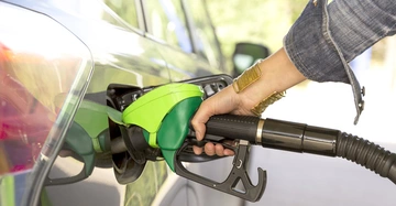 Eine Hand hält eine grüne Zapfpistole und tankt ein Auto in einer Tankstelle.