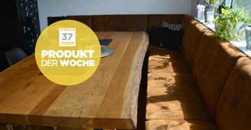 Ein großer Holztisch steht auf einem Leder-Sofa in einer gemütlichen Essbereich-Ecke. Text auf gelbem Kreis: 37 Produkt der Woche. Pflanzen und Tageslicht im Hintergrund.